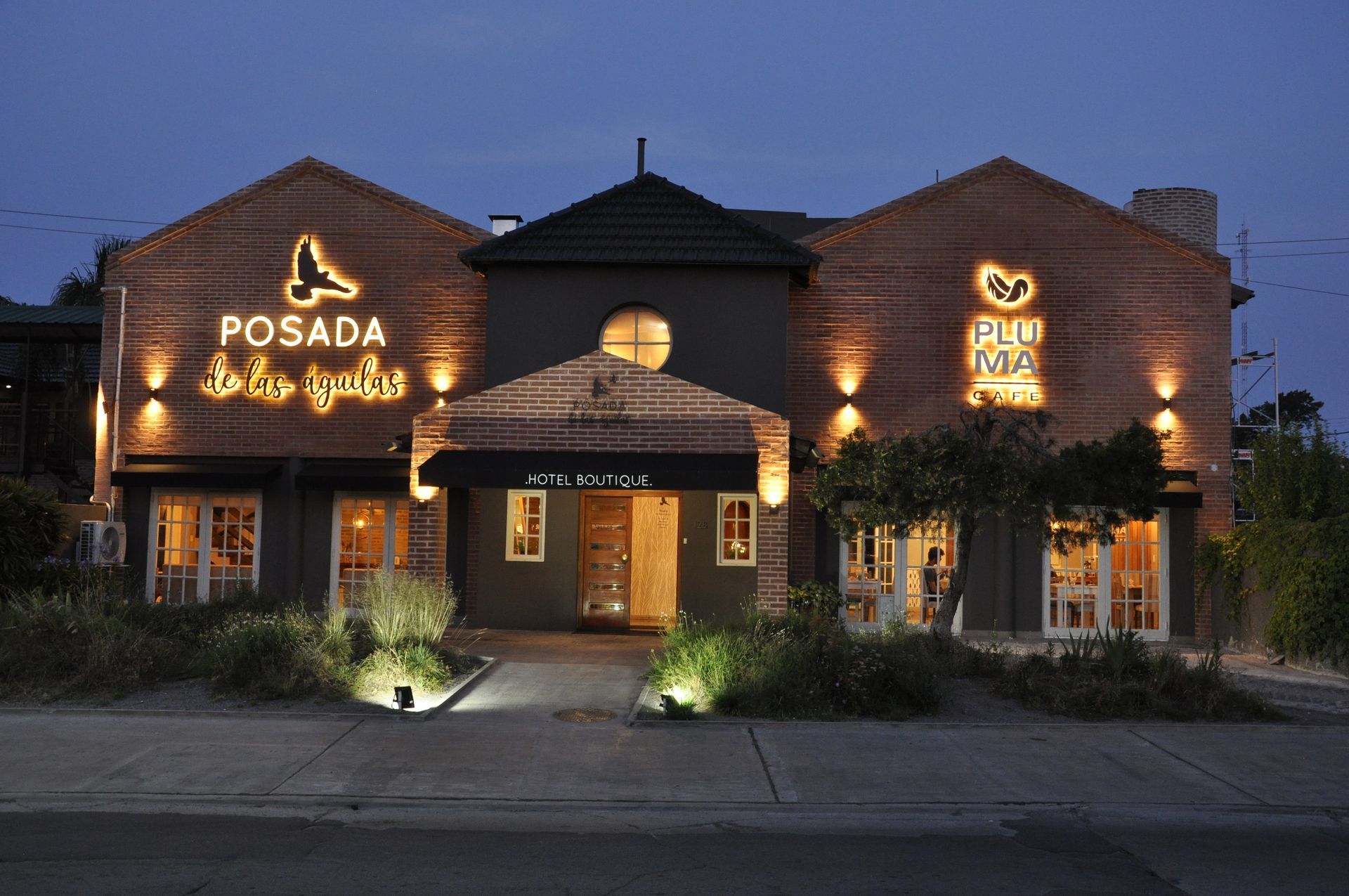 Vista nocturna del hotel Posada con cálidos letreros de neón y fachada de entrada iluminada.