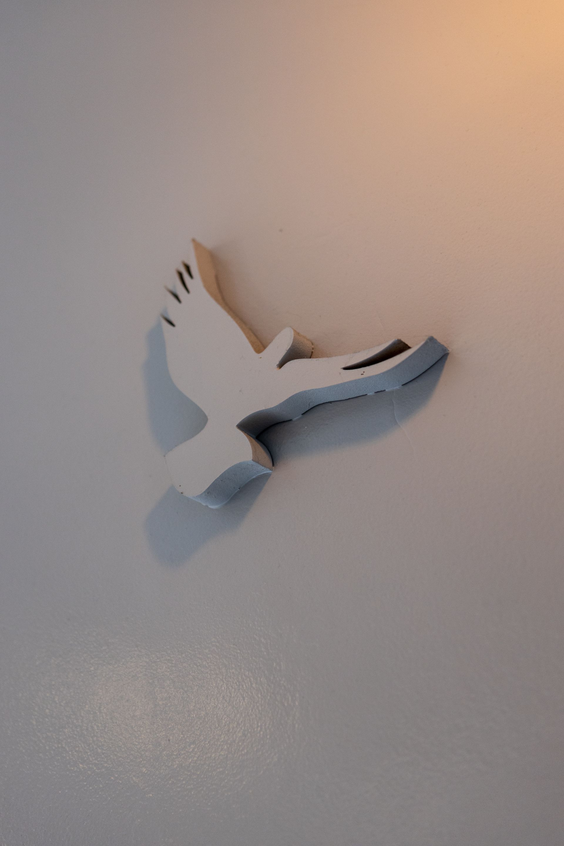 Decoración de pared con paloma blanca de alas azul grisáceas sobre fondo beige.