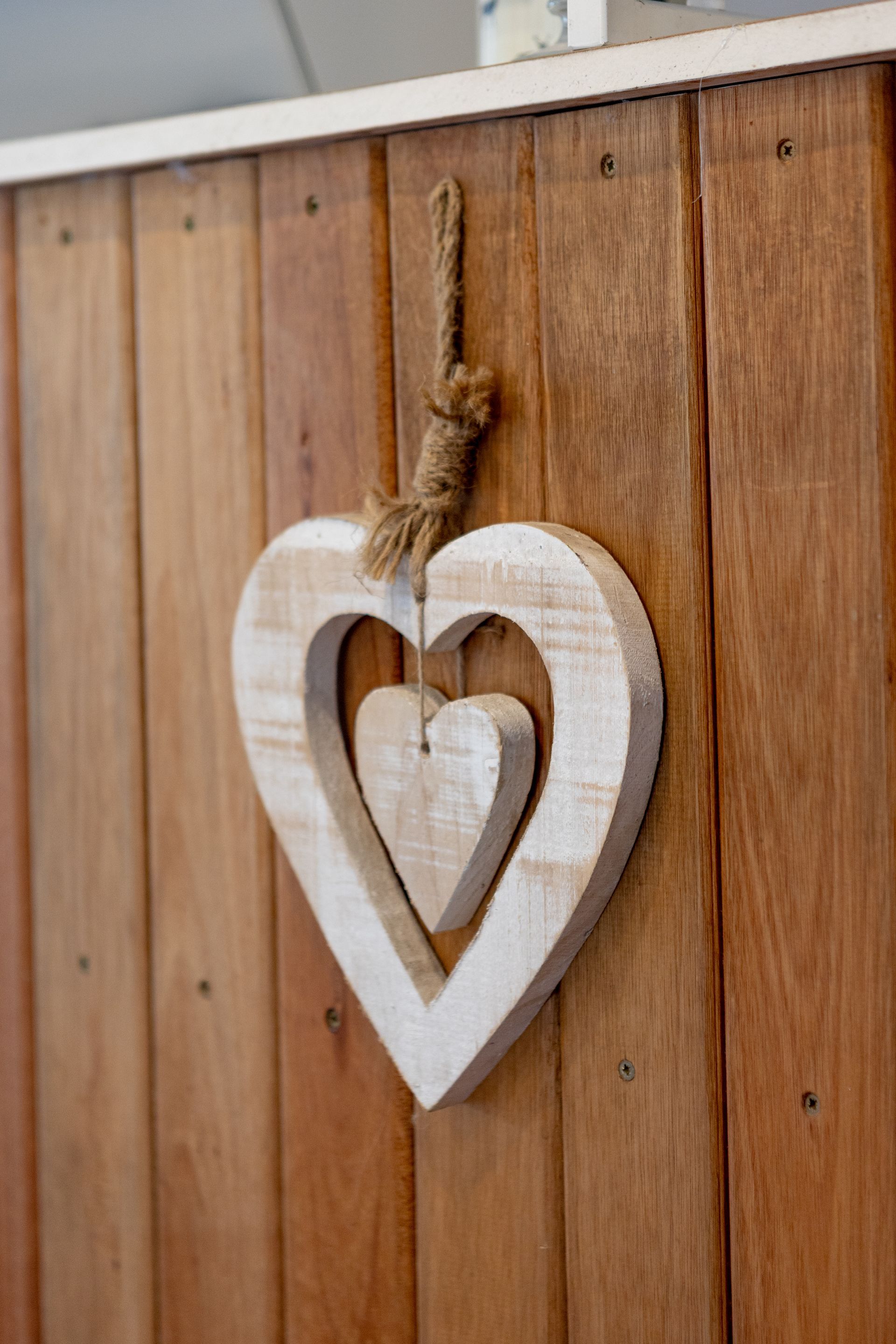 Adorno de corazón de madera blanca colgado en una valla de madera rústica vertical.