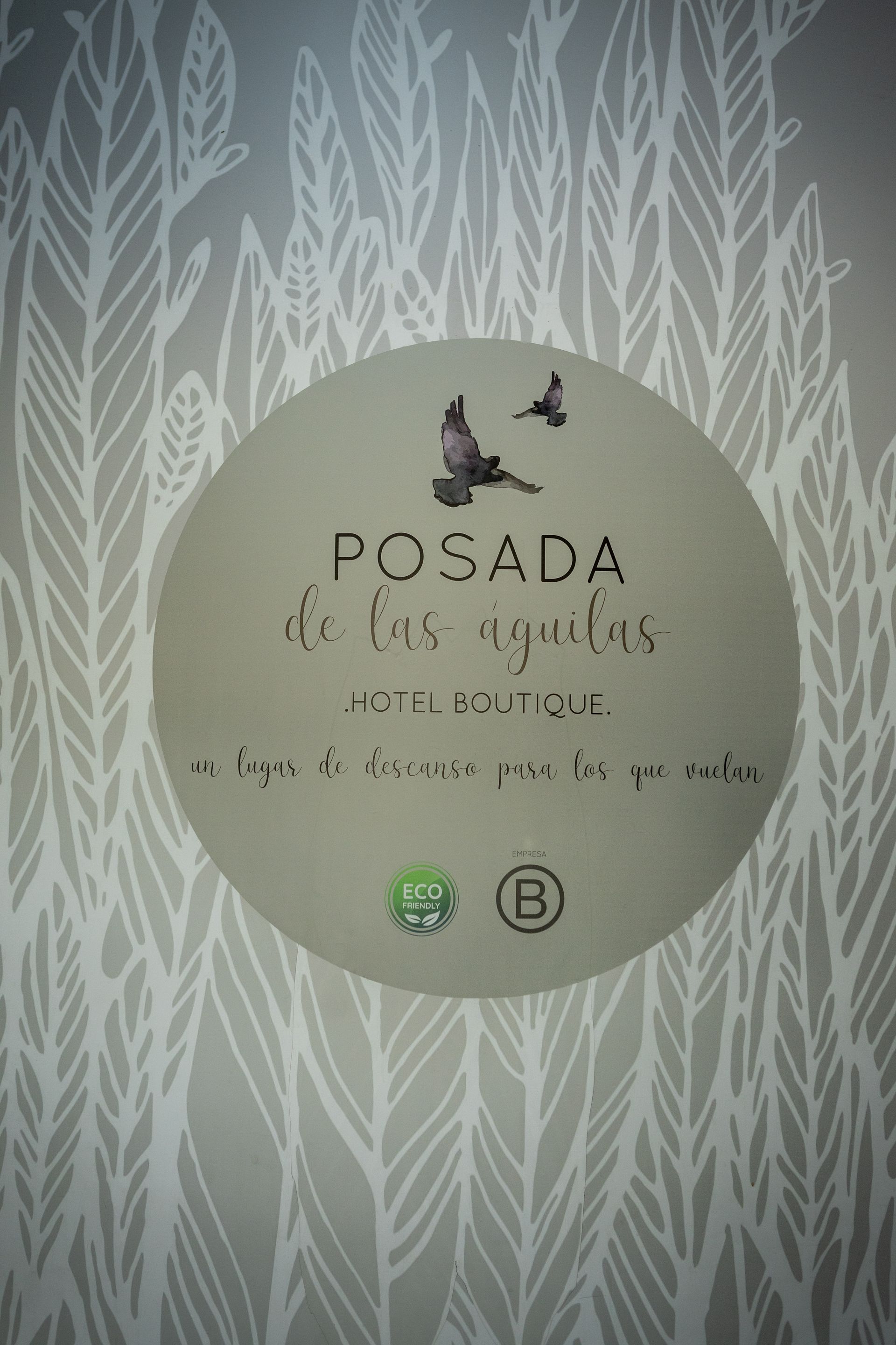 Logotipo circular de “Posada” sobre un fondo pálido con estampado de hojas y pequeñas siluetas de pájaros.