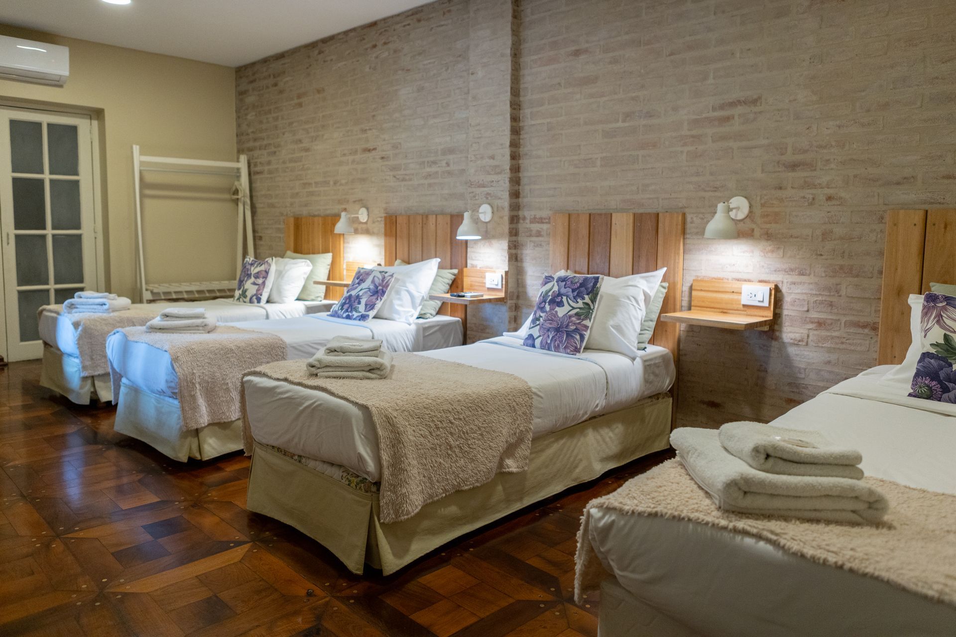 Una hilera de camas bien hechas en una luminosa habitación de hotel con lámparas de noche y toallas dobladas en cada cama.