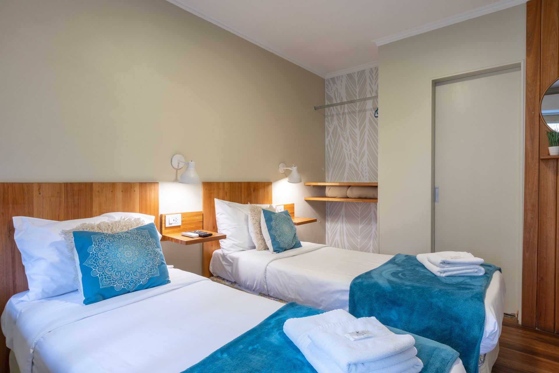 Habitación de hotel con dos camas individuales, detalles en azul, lámparas de noche y una pequeña zona de estar.