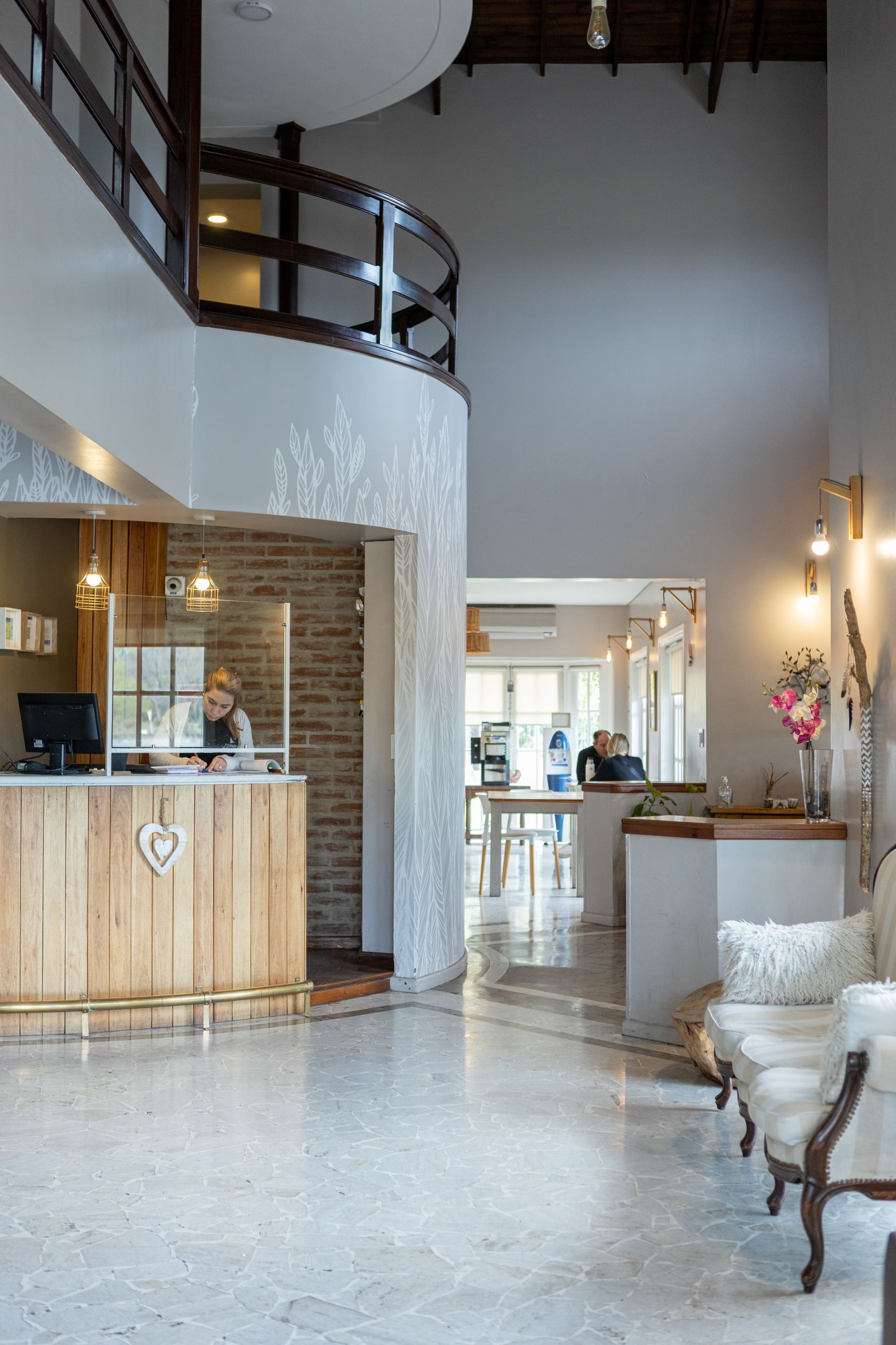 Vestíbulo de hotel moderno con escalera curva, mostrador de recepción de madera y suelo de hormigón pulido.