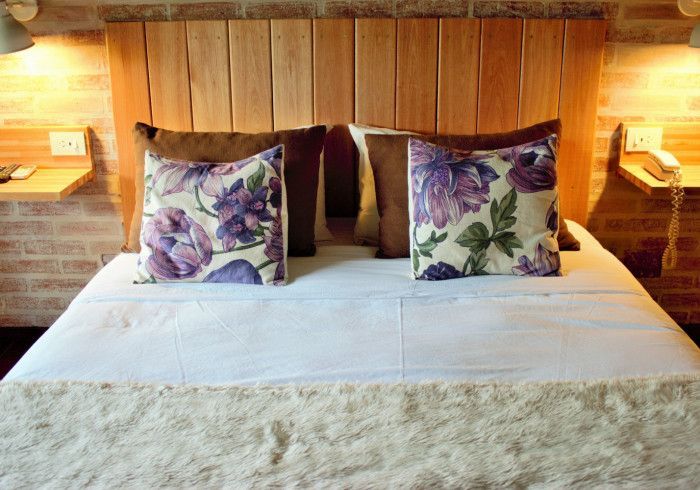 Cama acogedora con edredón blanco, cojines florales, cabecero de madera y lámparas de noche que proporcionan una luz cálida.