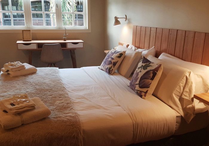 Habitación acogedora con una cama grande, toallas dobladas, almohadas estampadas y un asiento junto a la ventana.