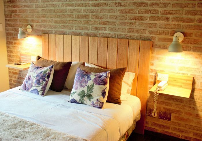 Acogedora habitación con cama de madera, cojines florales, ropa de cama blanca, pared de ladrillo visto y lámparas de noche.