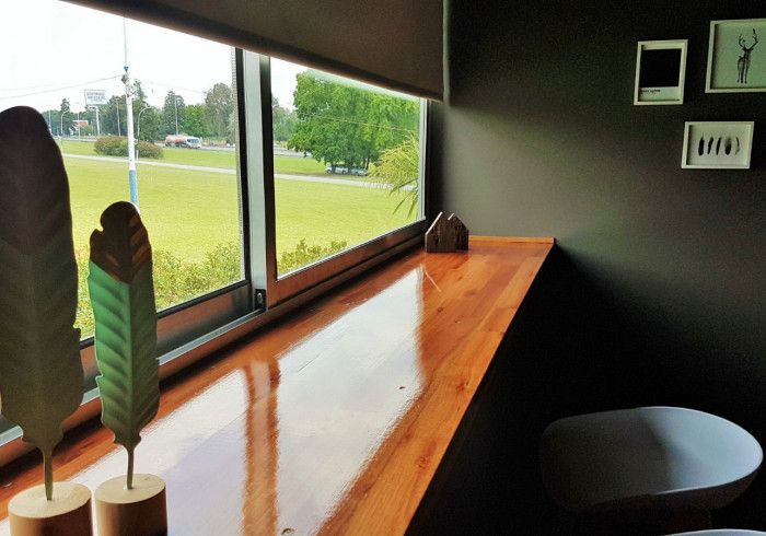 Rincón con asientos en el alféizar de madera, decorado con hojas y con vistas a un parque verde en el exterior.
