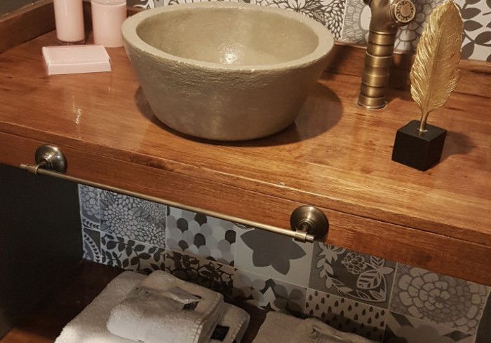Mueble de baño con lavabo de piedra sobre encimera de madera y azulejos estampados debajo.