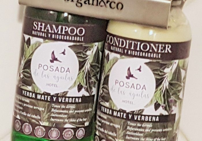Dos botellas de productos para el cuidado del cabello de la marca Posada, champú y acondicionador, con etiquetas moradas y hojas verdes, sobre un estante.