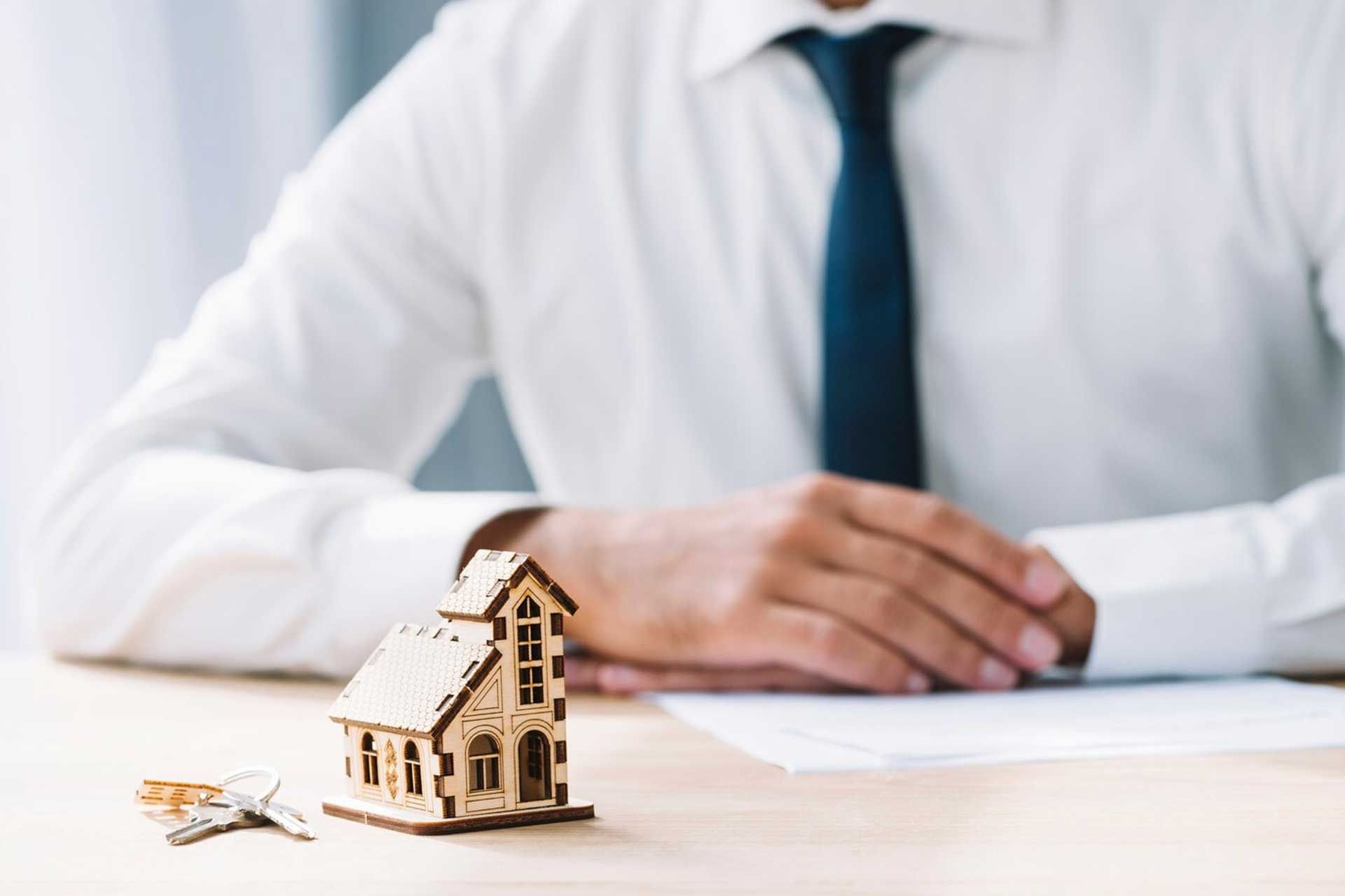A man is sitting at a table with a model house and keys.