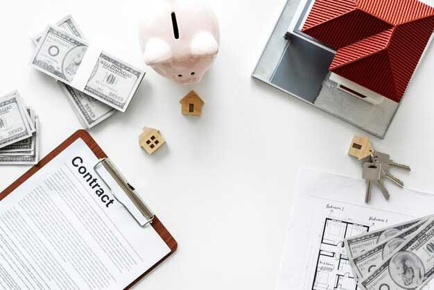 A piggy bank , a model house , keys , money and a contract on a table.