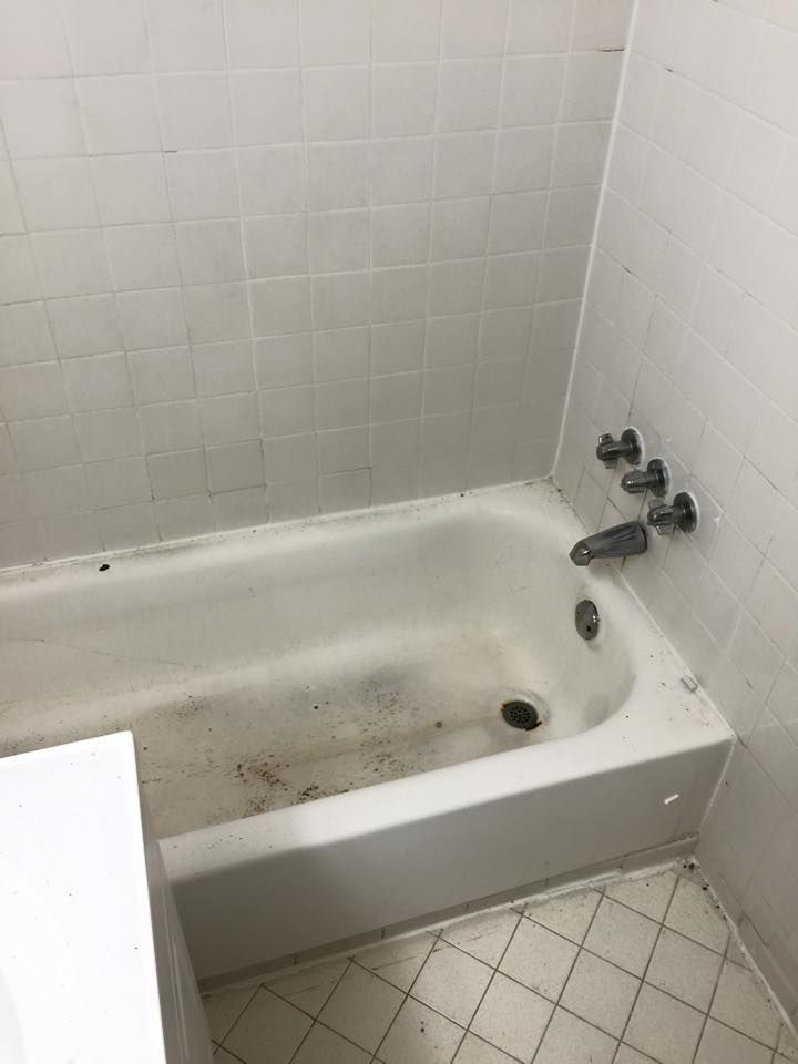 A dirty white bathtub and tiled walls in a bathroom.