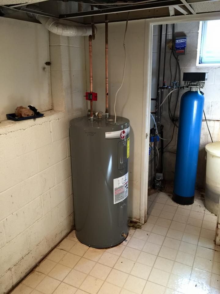 A gray water heater in a basement with copper pipes, a water softener, and tiled floor.