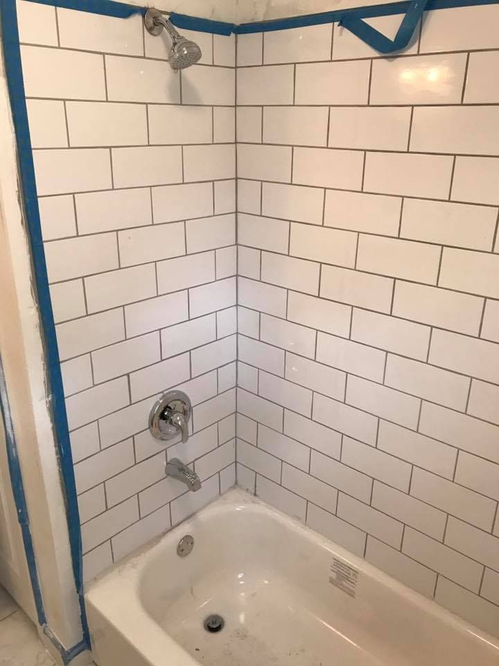 White tiled shower with a bathtub, showerhead, and faucet. Blue tape outlines the edges.