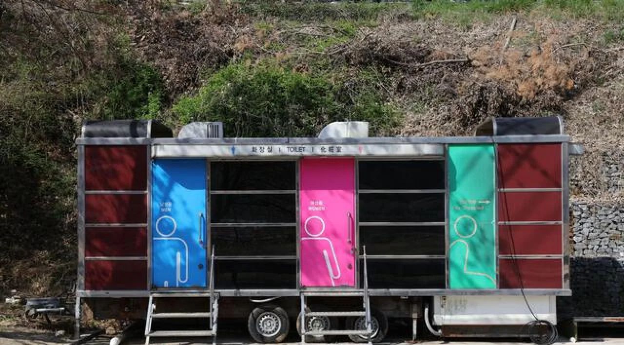 Trailer with blue, pink, and green panels parked on a road beside a rocky hillside.