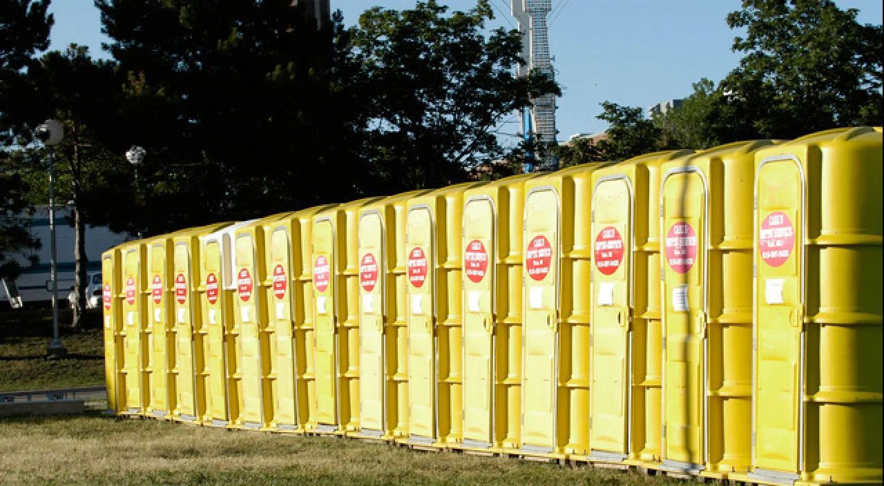 Row of yellow portable toilets with pink signs outdoors on a grassy lot