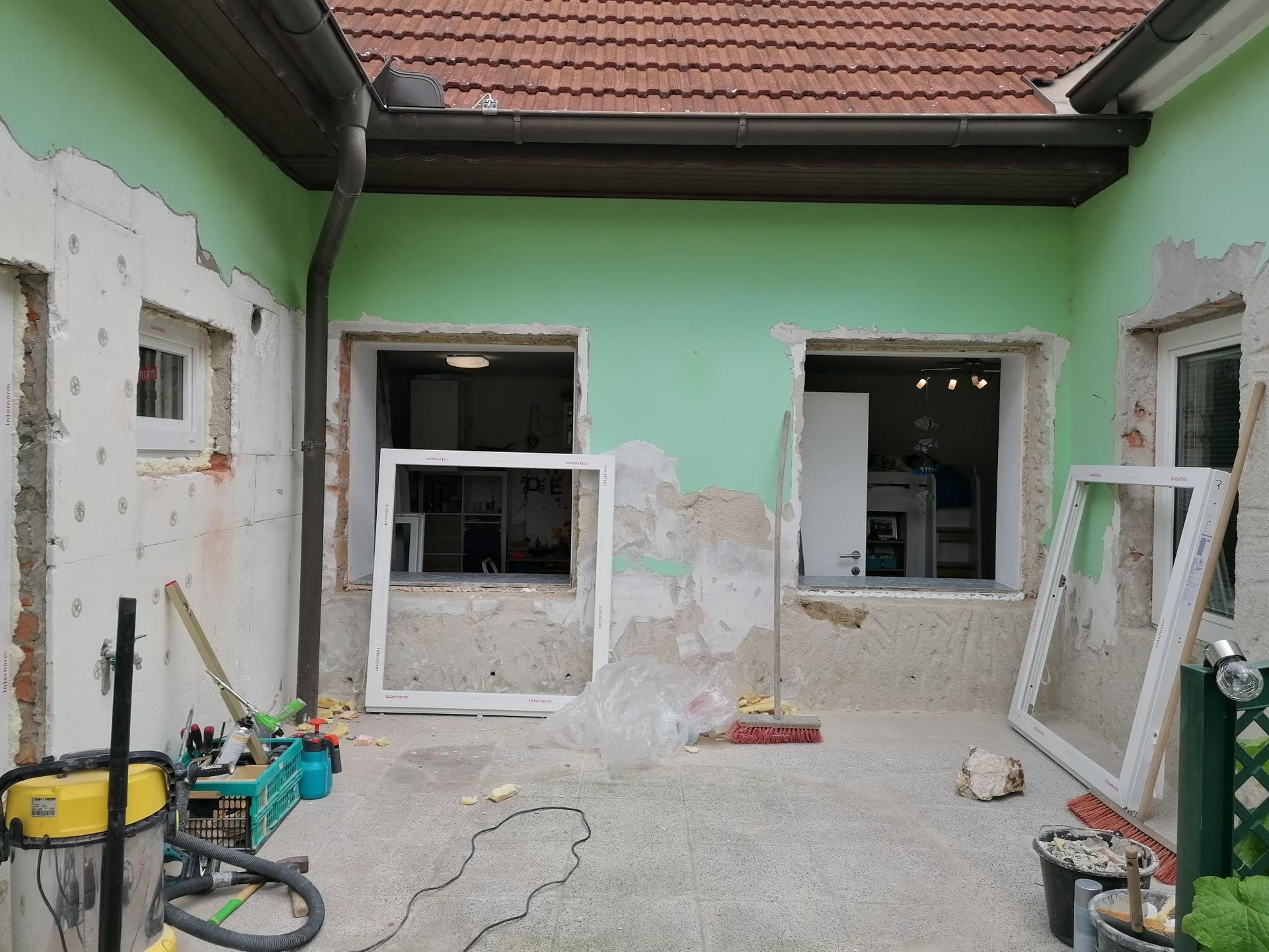 Fassade eines Gebäudes, das derzeit renoviert wird, mintgrüne Wände und an die Wand gelehnte neue Fensterrahmen.
