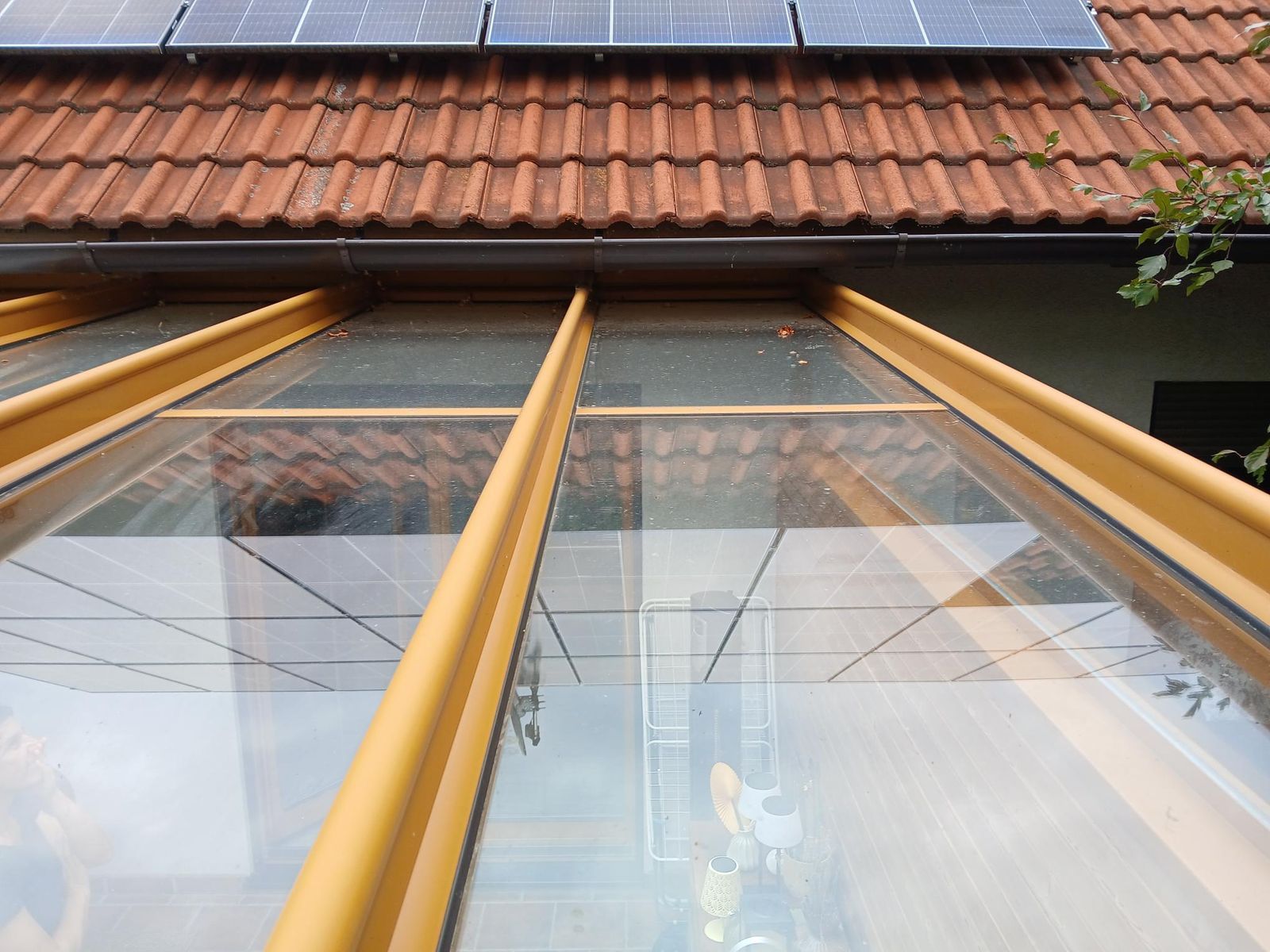 Unter einem mit Terrakotta-Ziegeln gedeckten Dach mit Solarpaneelen befindet sich eine überdachte Terrasse mit Glasdach