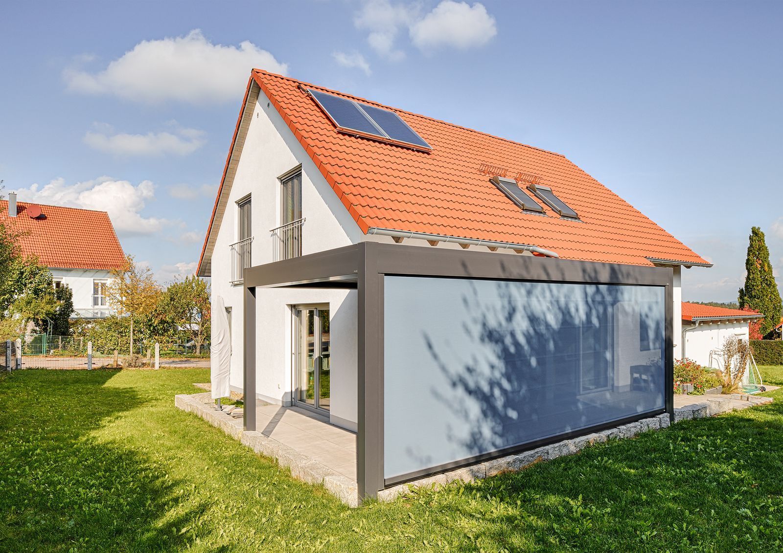 weißes zweistöckiges Haus mit rotem Ziegeldach und Solarpaneelen, mit überdachten Terrasse mit blauer Seitenwand.