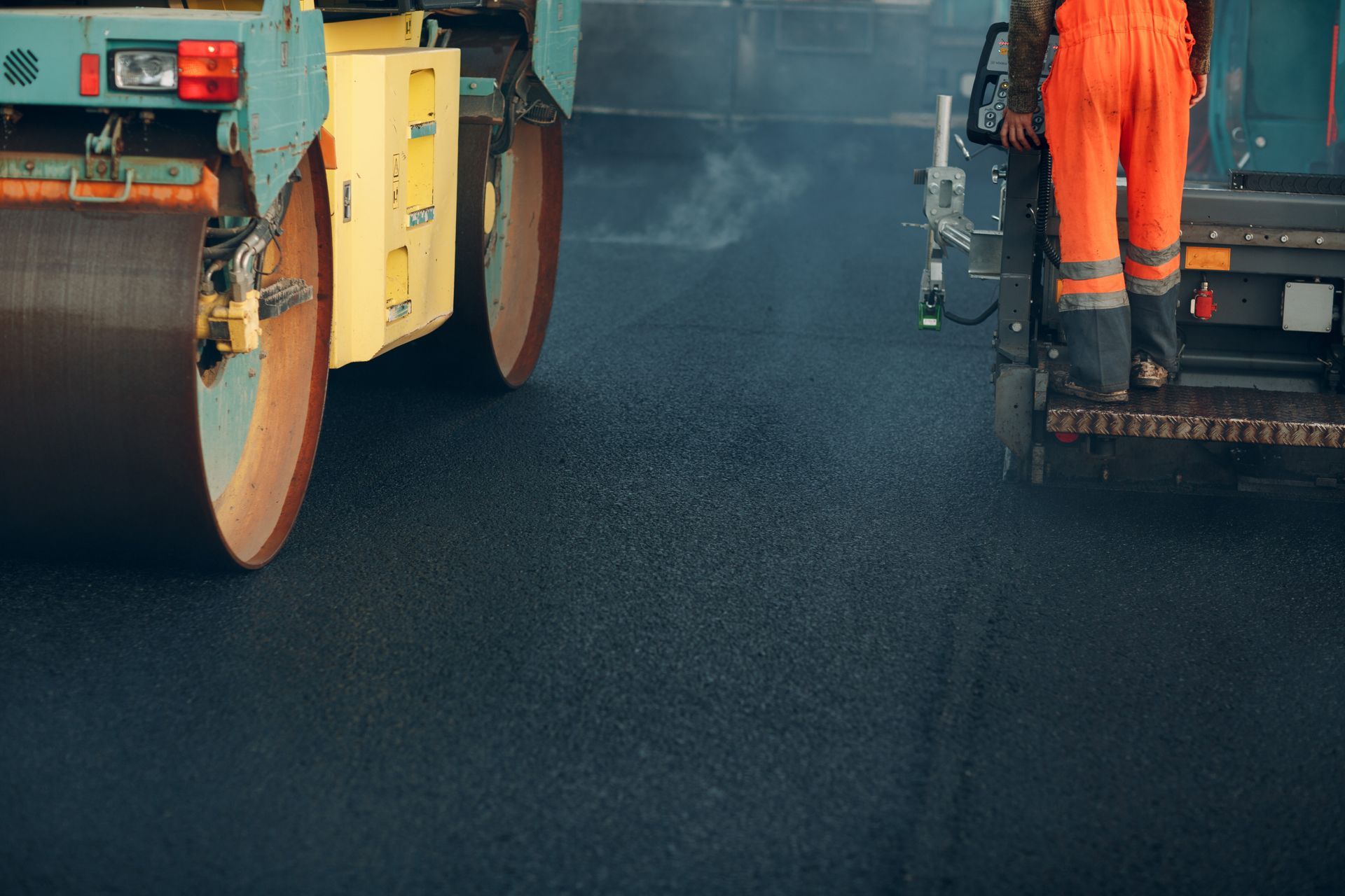 Fresh asphalt compacted by roller, worker in orange gear paving a smooth new road. Fresh asphalt compacted by roller, worker in orange gear paving a smooth new road.