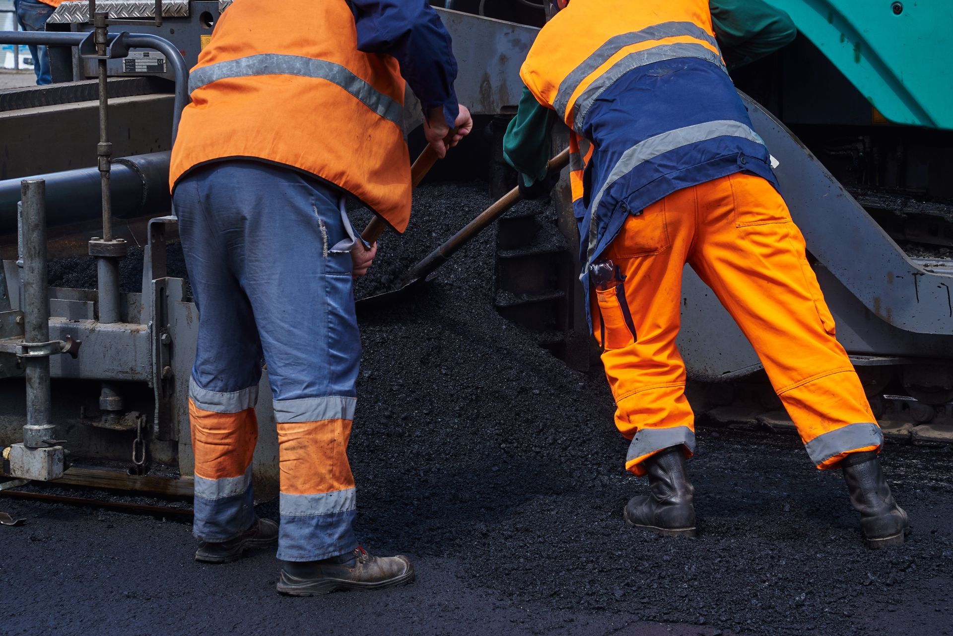 Road workers spreading and leveling hot asphalt behind a paving machine during road construction.