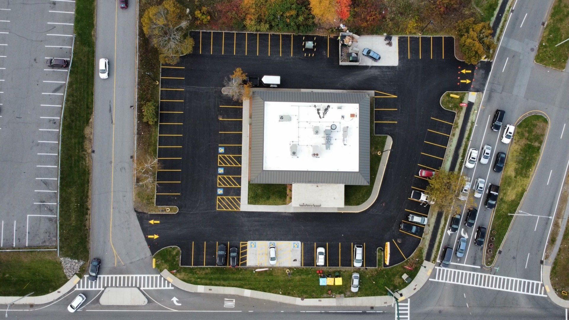 Aerial view of a rectangular commercial building with a surrounding parking lot and drive-thru lane near intersecting roads.