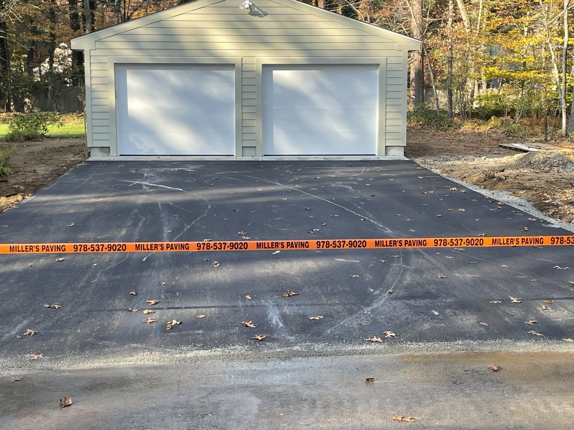 A light beige two-car garage at the end of a paved driveway, cordoned off by an orange construction barrier tape.