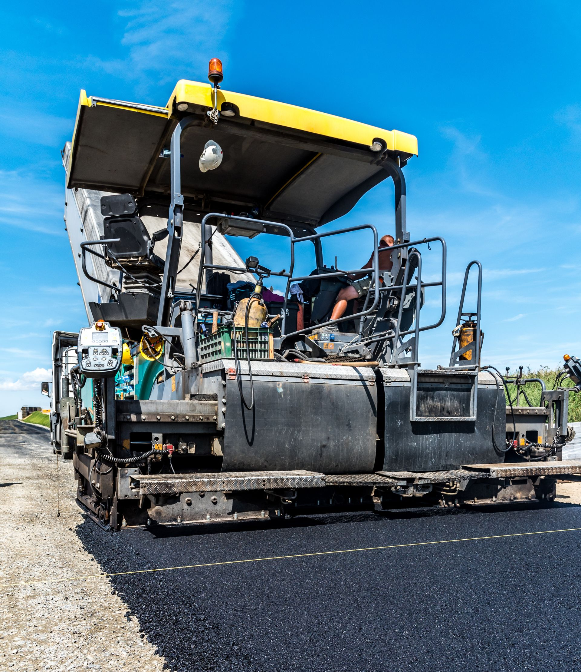 Paver machine laying fresh black asphalt on a road under a blue sky Paver machine laying fresh black asphalt on a road under a blue sky