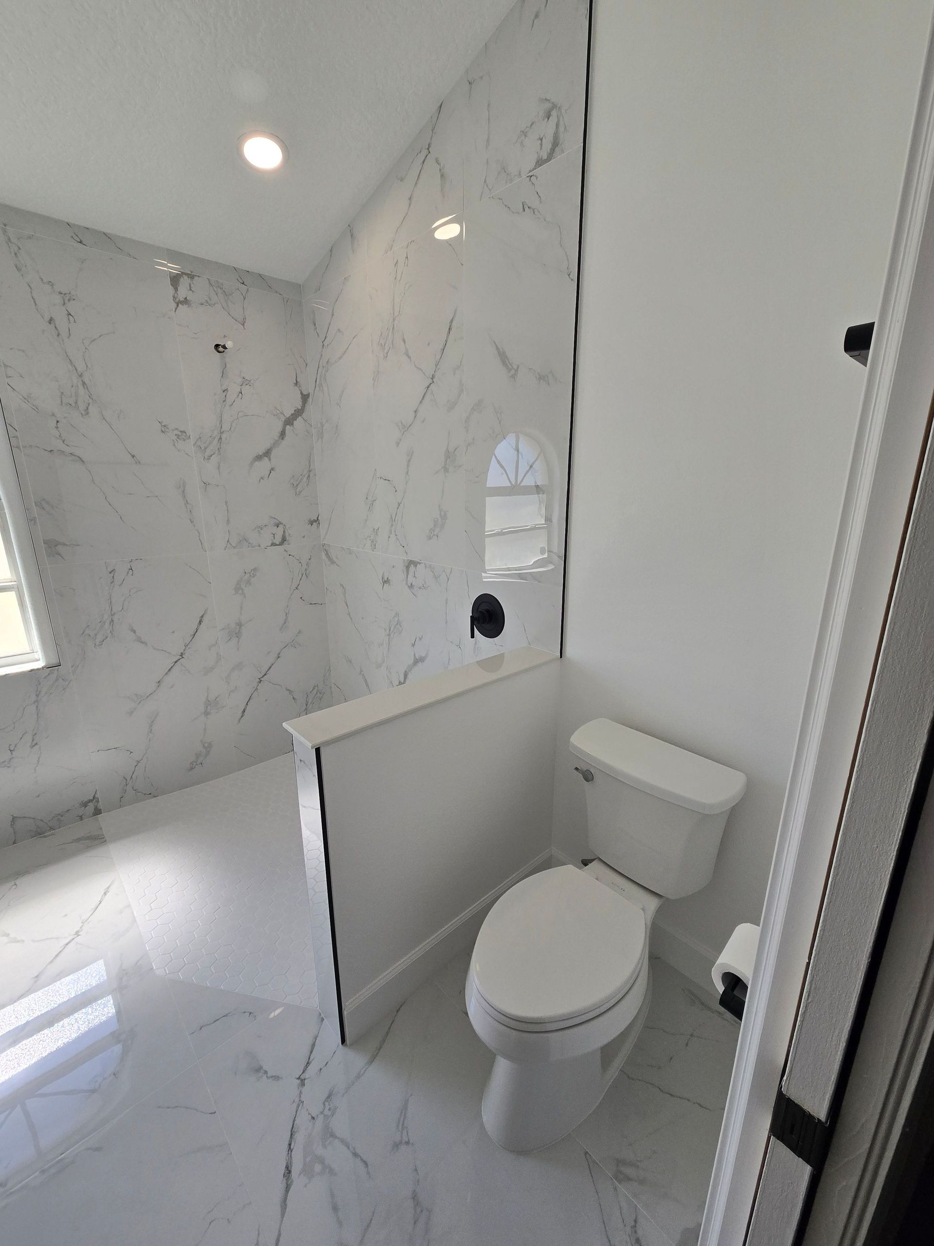 Small marble-tiled bathroom with a toilet, glass shower, and bright white walls.