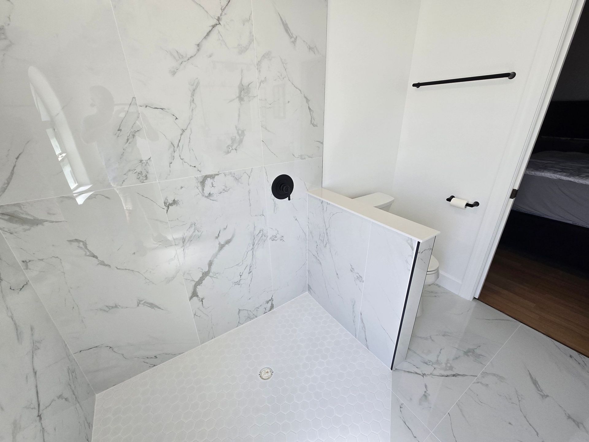 Marble bathroom shower with white tiled walls, glass door, and partially built partition wall