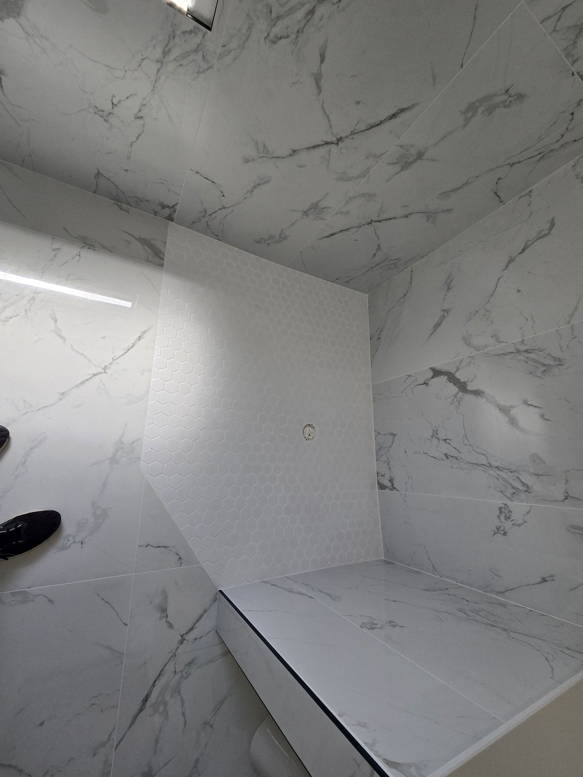 Marble-patterned white shower stall with bench and floor drain, viewed from above