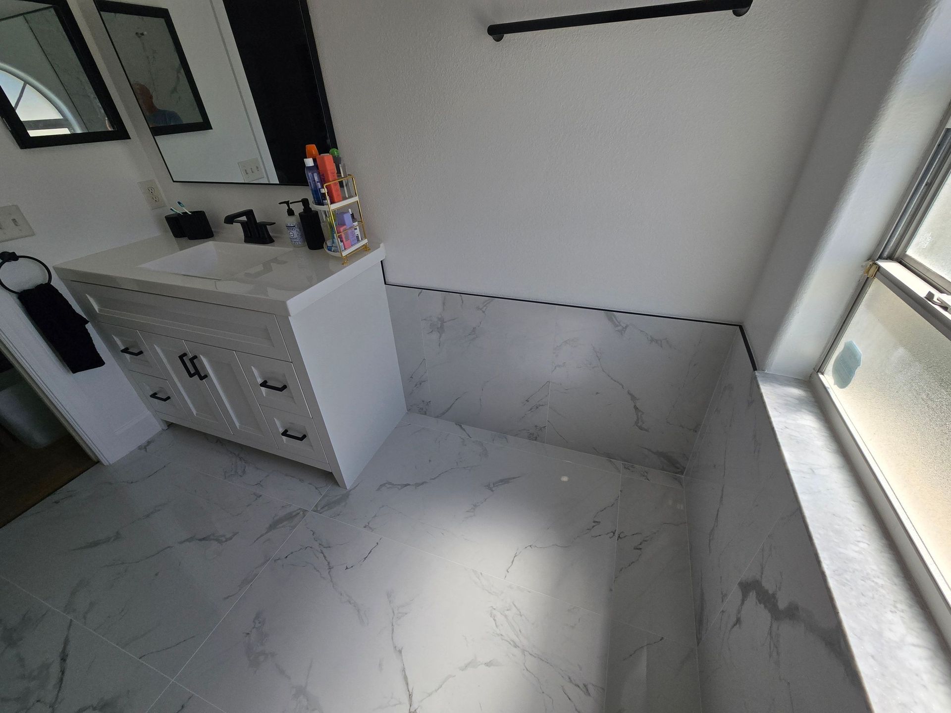 Modern bathroom with white marble tile floor, vanity sink, and large window light