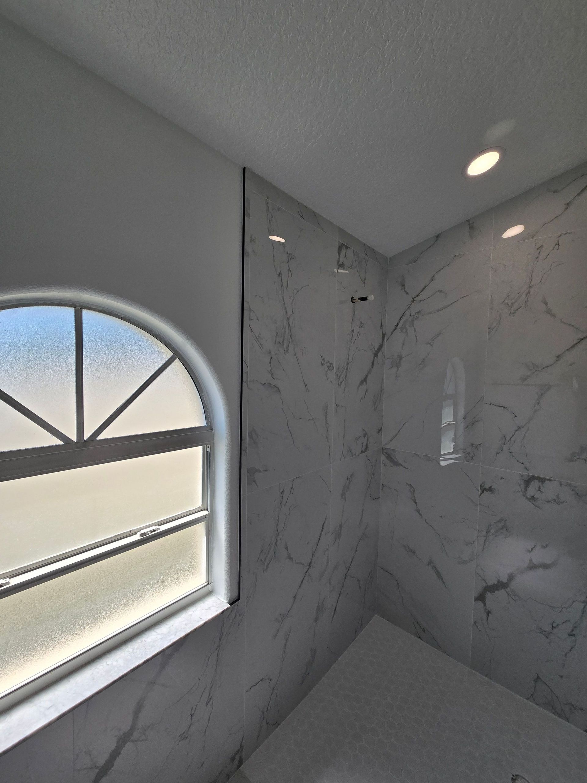 Small bathroom corner with marble-look walls, a window, and a recessed ceiling light.