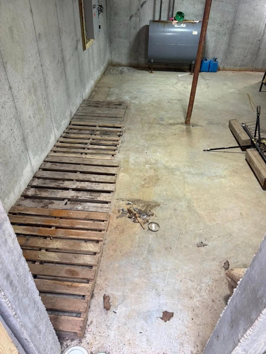 Concrete utility room with floor drain, wooden slatted trench, and a gray tank against the wall