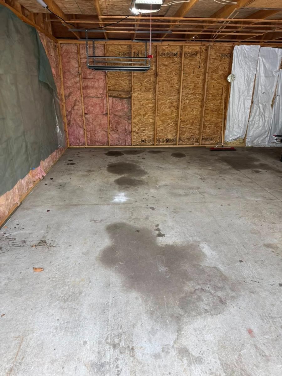 Unfinished garage interior with concrete floor, exposed insulation, and dark water stains.