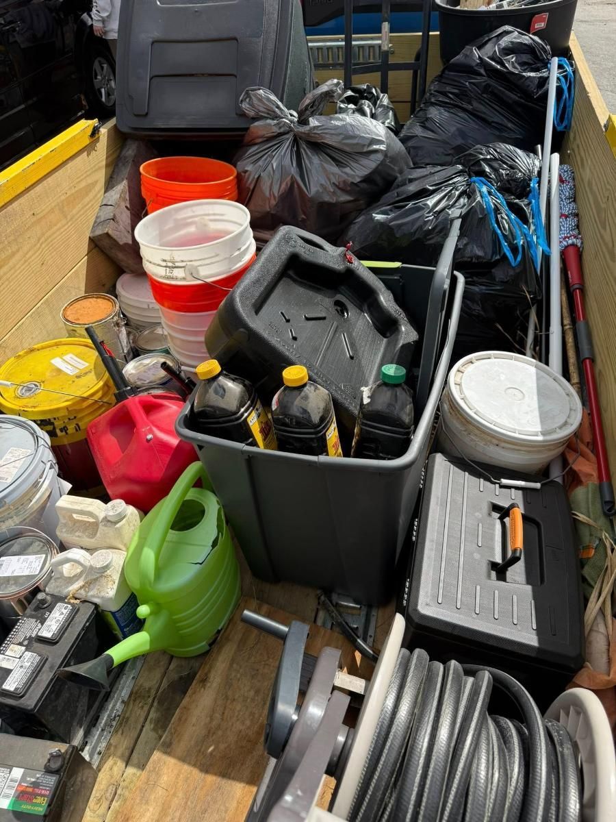 Assorted cleaning supplies and buckets piled in a truck bed, including hoses, containers, and toolboxes.
