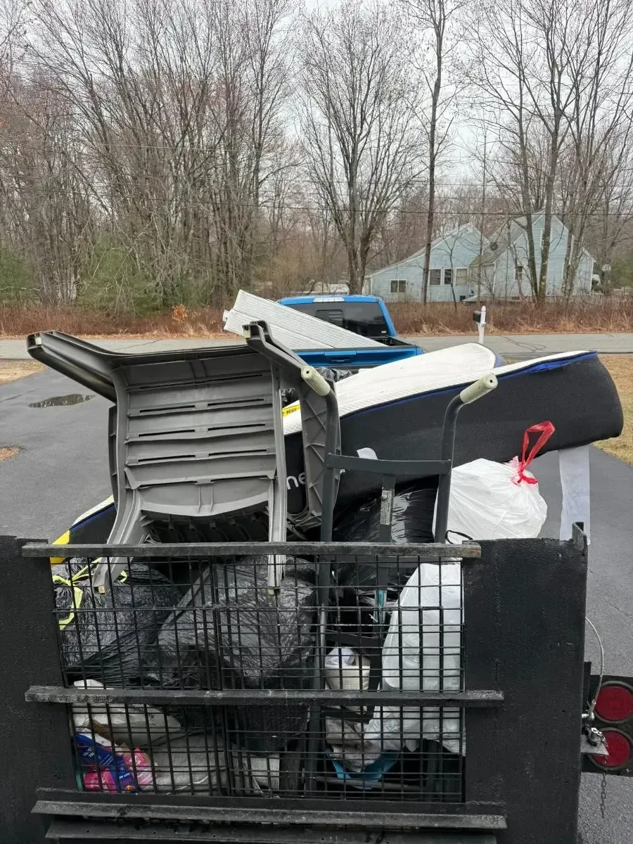 Overflowing cart of trash and stacked debris in a parking lot with leafless trees behind it