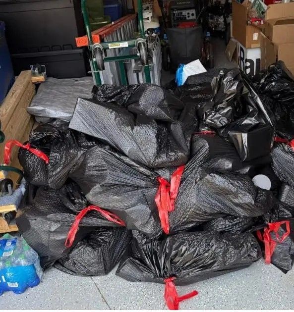 Pile of black trash bags tied with red straps in a garage or storage area