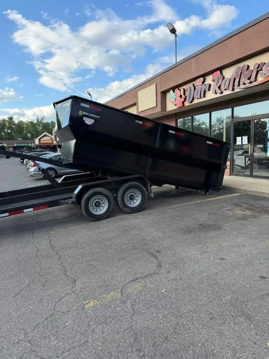 Black dump trailer parked outside a store with pink signage on a paved lot