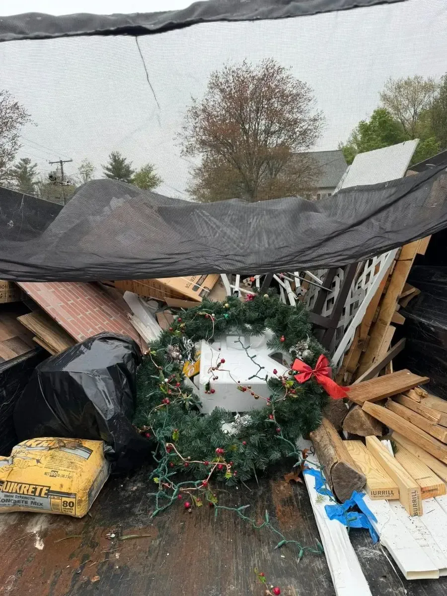 Collapsed outdoor shelter with debris, Christmas wreath, and a black tarp over broken wooden beams