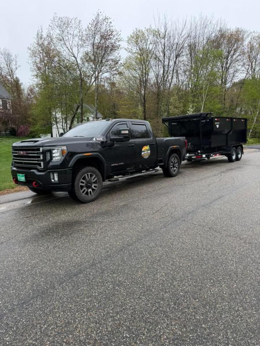 Black pickup truck towing a black trailer on a wet roadside with trees in the background
