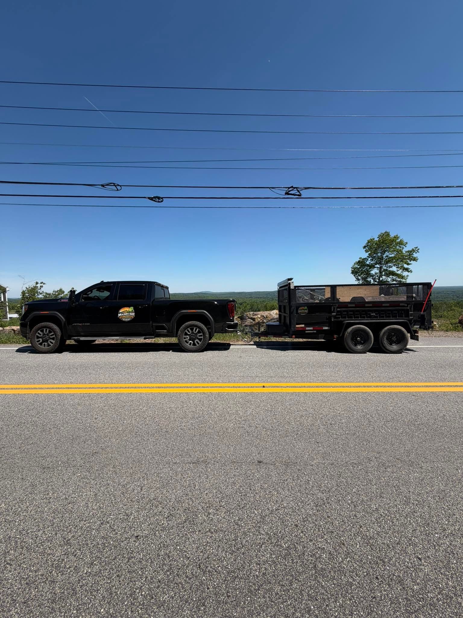 Black pickup truck towing a small trailer on a roadside under a clear blue sky.