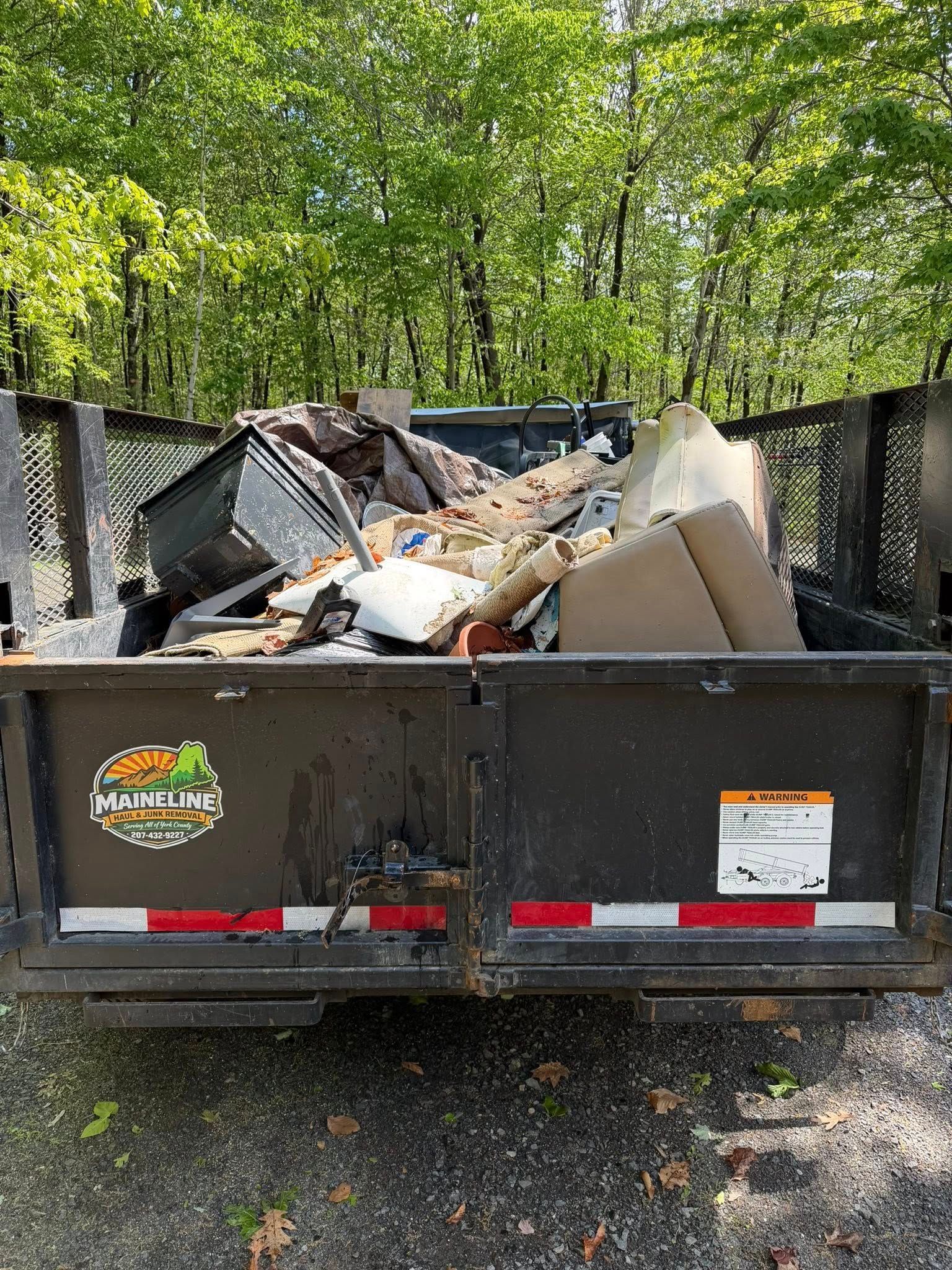 Dumpster overflowing with construction debris and cardboard in a wooded outdoor area