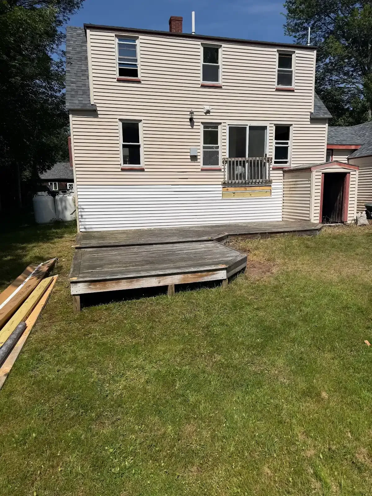 Back of a white two-story house with a small wooden deck and grassy yard, under renovation.