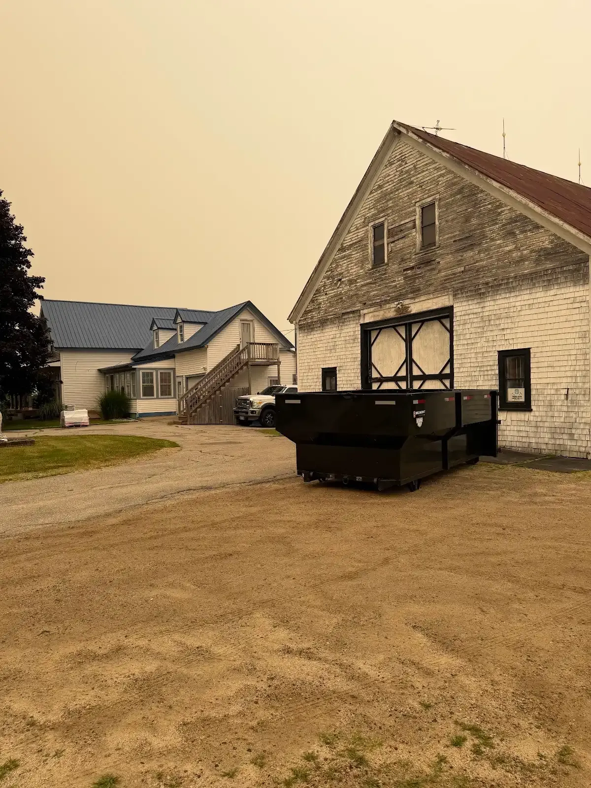 Historic stone building with dark dumpster in gravel lot under hazy sky
