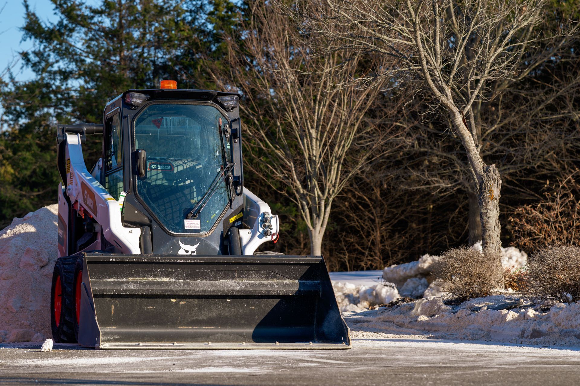 Snowplow clearing a snowy road, with trees and snowbanks in the background