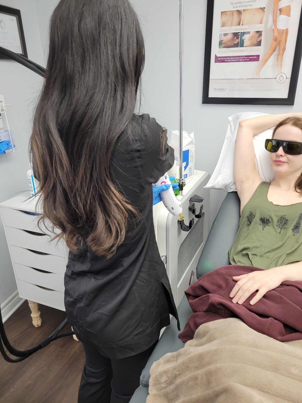 Woman in black standing beside a reclining patient wearing sunglasses in a clinical treatment room.