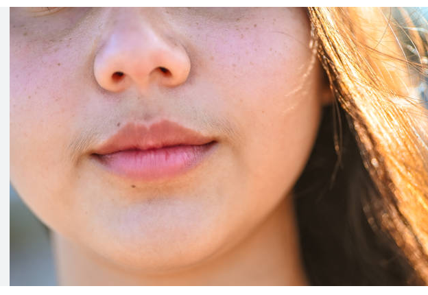 Close-up of a person's lower face in warm sunlight, with hair framing the cheeks.