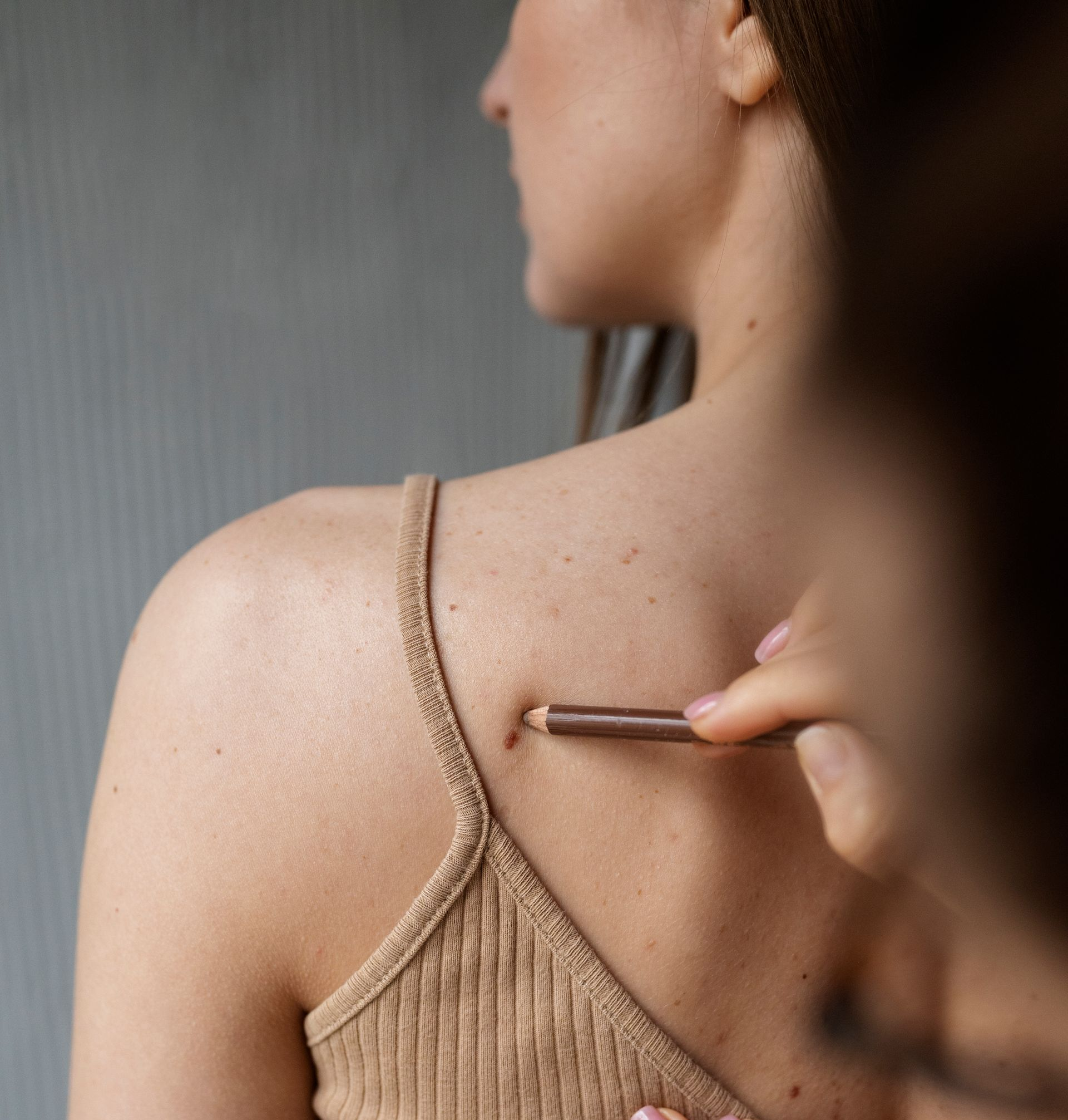 Person holding a small tool to the back of their shoulder, possibly checking a mole or skin spot
