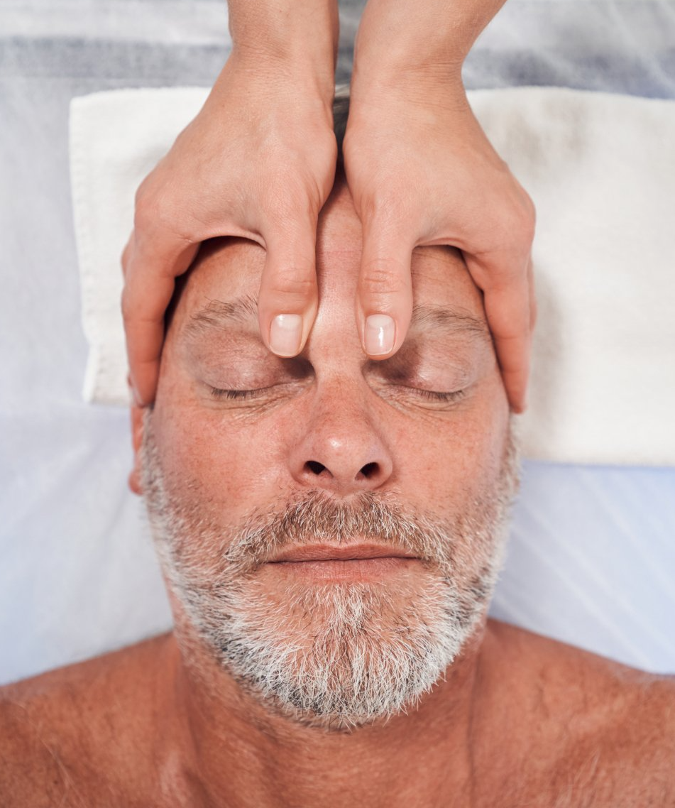 Hands massaging a man's forehead and temples as he lies with eyes closed on a treatment table